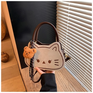 Dettaglio di una borsa beige a forma di gatto con ciondolo a forma di orsetto di peluche