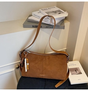 Detail van een bruine suède rechthoekige crossbodytas met kralenkwast en metalen logo-accent