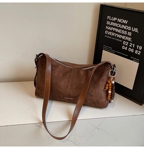 Detail van donkerbruine suède crossbody tas met houten kralenhanger en zilveren ritssluiting