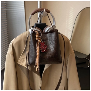 Detailed view of dark brown crocodile pattern bucket bag with bear and tassel charms