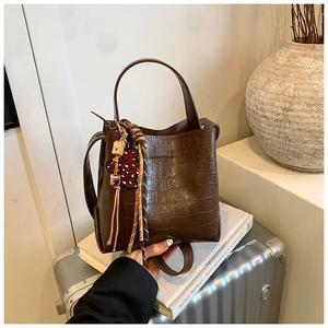 Detail of dark brown bucket bag with crocodile embossed texture and decorative charms