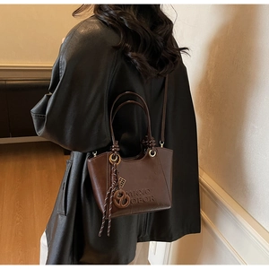 Détail du sac seau marron rétro montrant le logo embossé et l'ornement tissé latéral