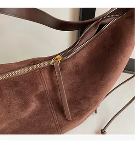 Close-up of smooth gold metal zipper and leather puller on a brown suede shoulder bag