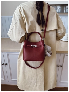 Détail d'un sac seau bordeaux en cuir grainé avec porte-clés ours sur un manteau beige