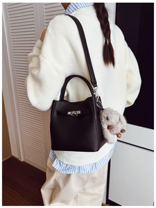 Modèle portant un sac seau noir en cuir litchi avec un charme lapin dans une pièce sobre