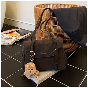 Détail d'un sac cabas en daim marron avec sangles décoratives et charmant ours en peluche