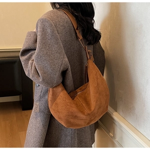 Detail view of brown suede hobo bag with contrast stitching on a model's shoulder