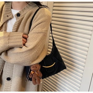 Detail of black dumpling bag featuring a gold crescent buckle and brown plush bear charm