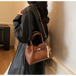 Gros plan sur un sac seau en cuir marron avec breloque en bois porté à l'épaule