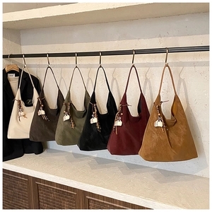 Row of large suede tote bags in various colors with woven tassel charms hanging on a metal rack
