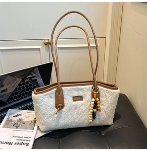 Detailopname van witte pluche draagtas met bruine leren handvatten en houten kralenhanger