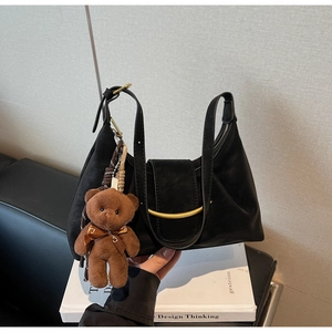 Detail of black dumpling bag with golden metal buckle and cute brown teddy bear charm