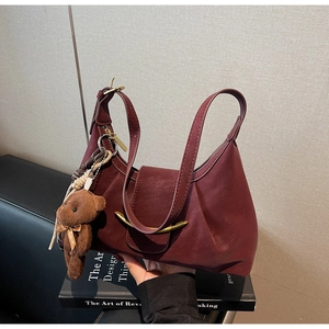 Detail of burgundy textured leather dumpling bag with gold metal buckle and bear charm