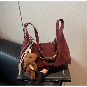 Detailed view of burgundy crescent dumpling bag with golden metal clasp and teddy bear charm