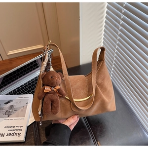 Detail of a brown leather dumpling bag featuring a golden ring and cute bear charm
