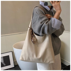 Chic cream tote bag with COFFEE tassel detail shown on shoulder in a minimalist setting