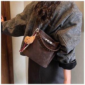 Detail of dark brown suede crossbody bag with braided handle and bear charm