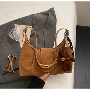 Detail of caramel leather dumpling bag with gold metal buckle and cute bear charm accessory