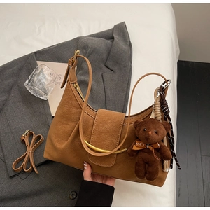 Detail view of brown pleated dumpling bag with golden ring decor and plush bear charm