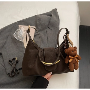 Detail of dark brown matte leather dumpling bag with crescent buckle and cute bear charm