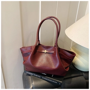 Close-up of burgundy woven tote bag with golden buckle on vintage book background