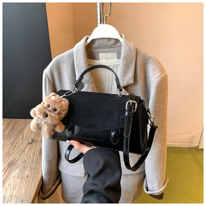 Detail der schwarzen matten Handtasche aus Lackleder mit einem süßen braunen Bärenanhänger