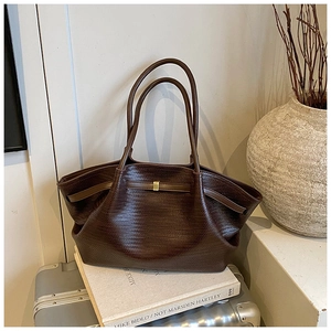 Detail of a dark brown woven tote bag featuring long leather straps and gold metal hardware