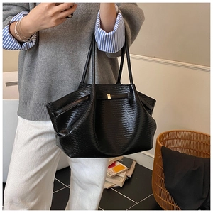 Close-up of black woven texture tote bag with golden metal buckle and smooth leather detail