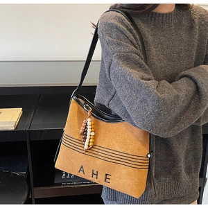 Detail view of brown suede tote bag featuring black embossed letters and ethnic beaded tassel