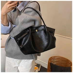 Detail of black woven shoulder bag showing large capacity and textured leather on a model