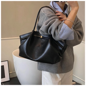 Detail of black woven tote bag featuring gold buckle accents and a bow strap design