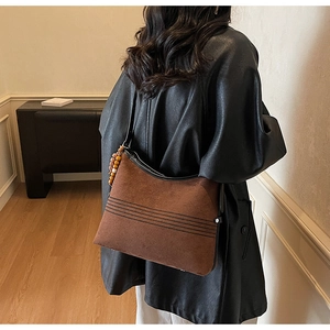 Close-up of brown suede tote bag featuring wooden bead charm and black leather shoulder strap