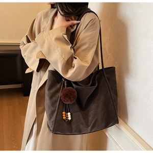 Close-up of vintage brown suede tote bag with decorative fur pompom and wooden beads detail