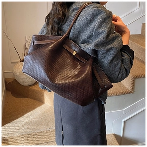 Detailed view of deep brown woven texture tote bag worn over the shoulder in indoor setting