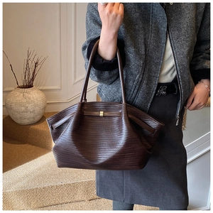 Close-up of a large dark brown woven tote bag with metallic buckle and long straps