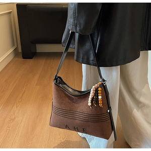 Close-up of brown suede tote bag featuring AHE embossed logo and colorful beaded tassel