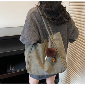 Close-up of olive green suede tote bag featuring a brown pom-pom and beaded charm detail