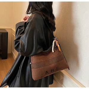 Detail view of dark brown faux suede tote featuring AHE embossed logo and colorful beaded strap