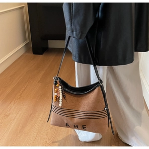 Detail of a brown suede tote bag with AHE logo, black stripes, and boho bead tassel charm