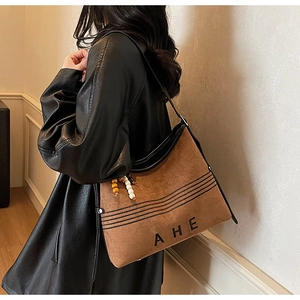 Detail view of caramel brown suede tote bag featuring bead tassels and AHE logo
