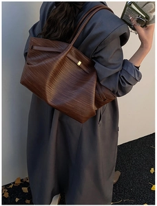 Detail of a dark brown pleated tote bag with fine woven texture and gold metal buckle