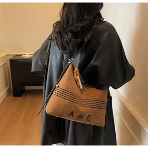 Detailed view of brown suede tote bag featuring black leather straps and wooden bead charm
