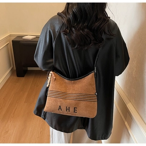 Detail of brown suede tote bag with black stripes, AHE logo and wooden bead charm accessory