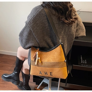 Detail of ginger suede tote bag featuring black AHE embroidery and beaded charm