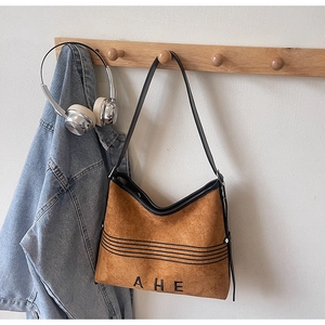 Detail of a brown faux suede tote bag with black letter branding on a wooden hook