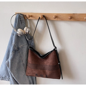 Close-up of brown suede tote bag featuring AHE embroidery and black leather straps