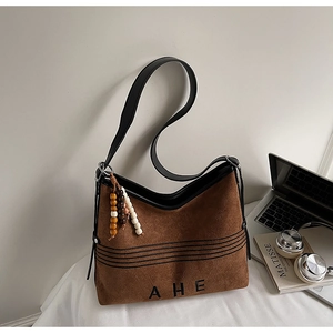 Detail view of brown suede tote bag featuring AHE embroidery and stylish beaded charm