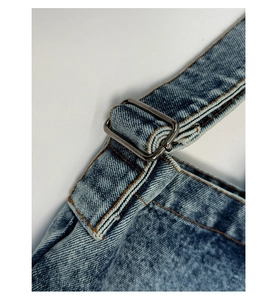 Détail de la boucle métallique réglable et coutures jaunes sur bandoulière en jean
