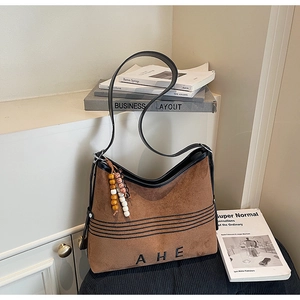 Close-up of brown suede tote bag with black AHE lettering and beaded tassel detail