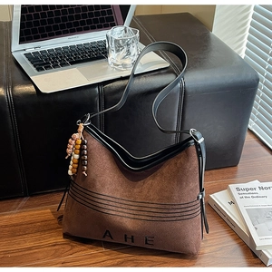 Detail of vintage brown suede tote bag featuring a leather strap and a beaded tassel charm